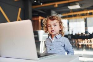 Smart child in casual clothes using laptop for education purposes or fun photo