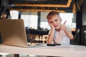 niño inteligente en ropa casual con computadora portátil en la mesa diviértete foto