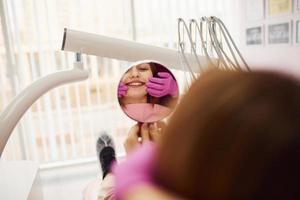 mira al espejo. niña visitando al dentista en la clínica. concepción de la estomatología foto