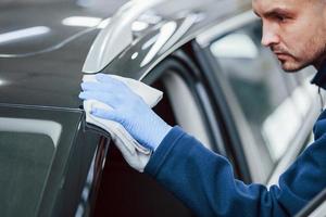 Male worker in uniform polishing new modern car. Conception of service photo