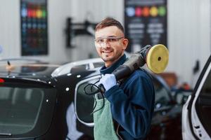 Male worker in uniform polishing new modern car. Conception of service photo