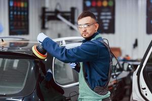 trabajador masculino en uniforme puliendo un coche nuevo y moderno. concepto de servicio foto