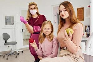 niña visitando al dentista en la clínica con su madre. concepción de la estomatología. sosteniendo manzanas foto