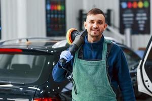 trabajador masculino en uniforme puliendo un coche nuevo y moderno. concepto de servicio foto