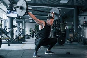 Strong young man in sportive clothes doing exercises with heavy weights in the gym photo