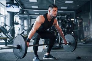 Strong young man in sportive clothes doing exercises with heavy weights in the gym photo