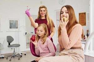 Little girl visiting dentist in clinic with her mom. Conception of stomatology. Holding apples photo