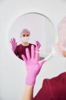 Young female dentist in uniform standing in stomatology office befor mirror photo