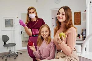 Little girl visiting dentist in clinic with her mom. Conception of stomatology. Holding apples photo