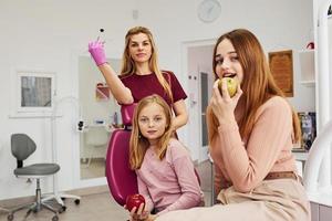 Little girl visiting dentist in clinic with her mom. Conception of stomatology. Holding apples photo