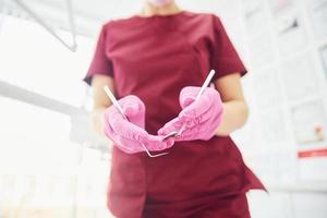 Close up view of female dentist in uniform that standing in stomatology office with tools in hands photo