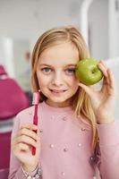 Holding brush and green apple. Little girl visiting dentist in clinic. Conception of stomatology photo