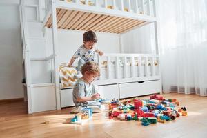 Two little boys have fun indoors in the bedroom with plastic construction set photo