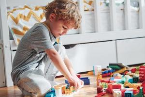 Cute little boy sitting and have fun indoors in the bedroom with plastic construction set photo