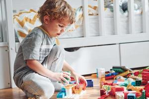 Cute little boy sitting and have fun indoors in the bedroom with plastic construction set photo