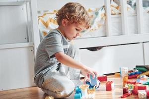 Cute little boy sitting and have fun indoors in the bedroom with plastic construction set photo
