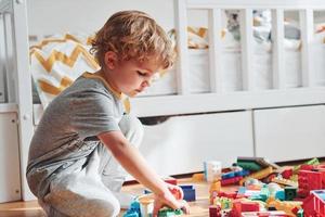 Cute little boy sitting and have fun indoors in the bedroom with plastic construction set photo