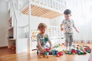 Two little boys have fun indoors in the bedroom with plastic construction set photo