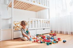 Cute little boy sitting and have fun indoors in the bedroom with plastic construction set photo