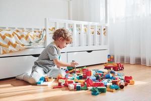 Cute little boy sitting and have fun indoors in the bedroom with plastic construction set photo