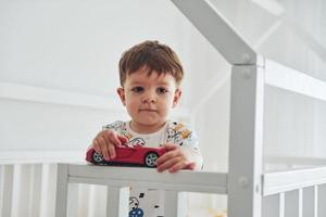 Cute little boy resting and have fun with car indoors in the bedroom photo