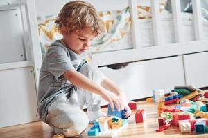 Cute little boy sitting and have fun indoors in the bedroom with plastic construction set photo