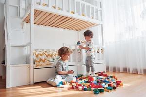 Two little boys have fun indoors in the bedroom with plastic construction set photo