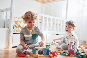 Two little boys have fun indoors in the bedroom with plastic construction set photo