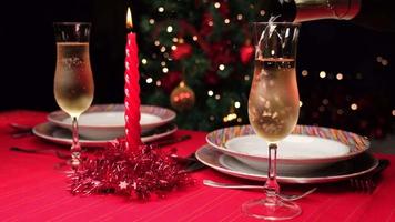 Champagner auf einen weihnachtlich dekorierten roten Tisch gießen. Abendessen zu Hause oder im Restaurant