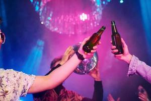 celebrando y golpeando botellas con alcohol. los jóvenes se divierten en el club nocturno con luces láser de colores foto