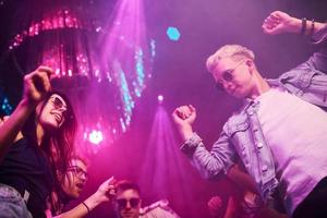 View from below of young people that having fun in night club with colorful laser lights photo