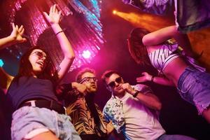 View from below of young people that having fun in night club with colorful laser lights photo