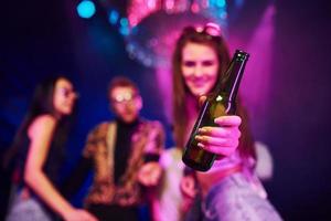 Girl holding bottle. Young people is having fun in night club with colorful laser lights photo