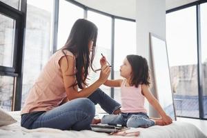 aprendiendo a maquillarme. joven madre con su hija pasando el fin de semana juntos en la habitación foto