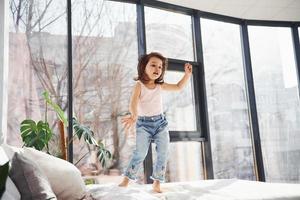 Cute little girl at home alone. Having fun by jumping on the bed photo