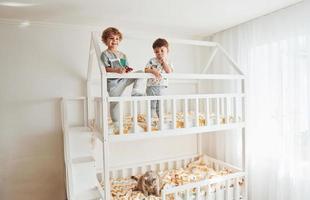 dos niños pequeños descansan y se divierten juntos en el interior del dormitorio foto