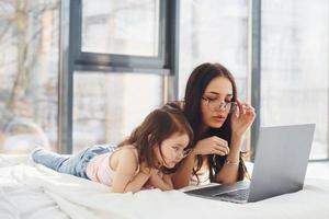 joven madre con su hija pasando el fin de semana juntos en la habitación y usando una laptop foto