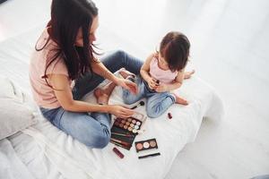 aprendiendo a maquillarme. joven madre con su hija pasando el fin de semana juntos en la habitación foto