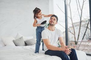 Happy father with his daughter having fun with comb at home together photo