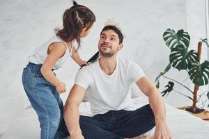 Little girl wearing crown on the father's head. Having fun at home together photo