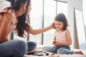 aprendiendo a maquillarme. joven madre con su hija pasando el fin de semana juntos en la habitación foto