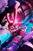 View from below of young people that having fun in night club with colorful laser lights photo