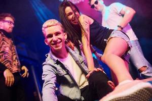 volviéndose locos y posando juntos para la cámara. los jóvenes se divierten en el club nocturno con luces láser de colores foto