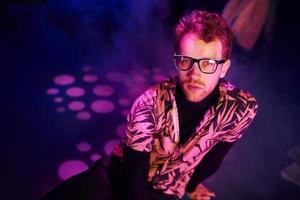 Young man in glasses have fun inside of night club with pink lightings photo