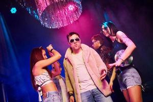 Elegant man in sunglasses in the midle feels like a boss. Young people is having fun in night club with colorful laser lights photo