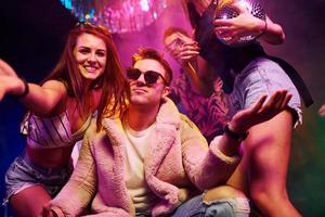 Elegant man in sunglasses in the midle feels like a boss. Young people is having fun in night club with colorful laser lights photo