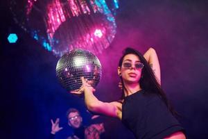 hermosa joven diviértete, bailando en el club nocturno. sosteniendo la pelota de fiesta foto