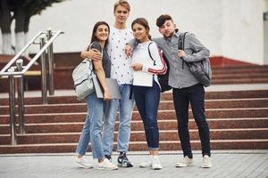 posando para una cámara. grupo de jóvenes estudiantes con ropa informal cerca de la universidad durante el día foto