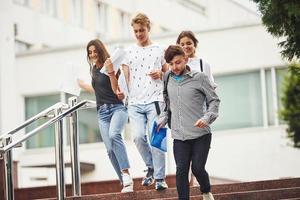 Walking on the stairs. Group of young students in casual clothes near university at daytime photo
