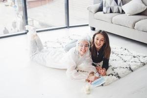 Two young female friends lying down on the floor of domestic room. One of them in lab coat photo